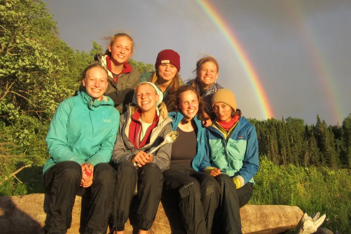 Seven teens sitting under a double rainbow