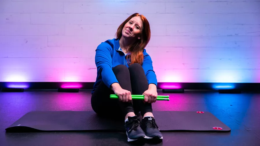 Kimberly Cooper sits with drumsticks on a yoga mat smiling