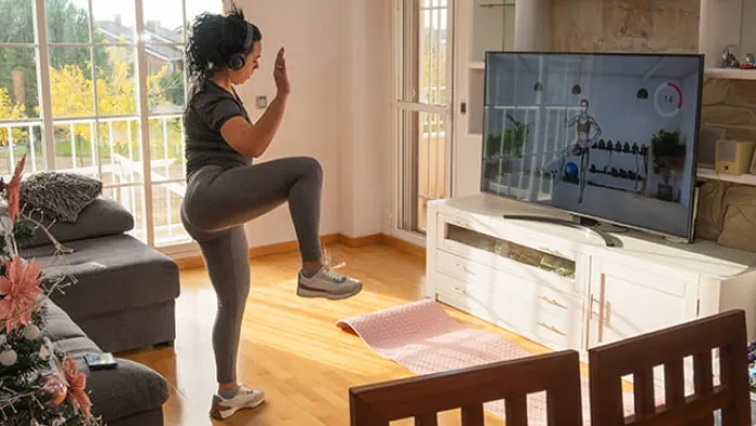 Woman exercising at home, following a live-streamed fitness class on her device.