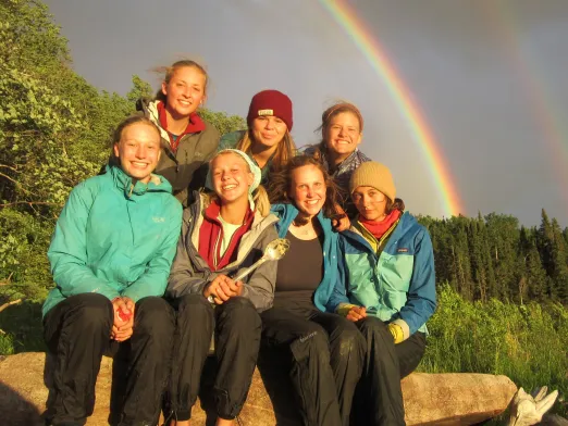 Seven teens sitting under a double rainbow